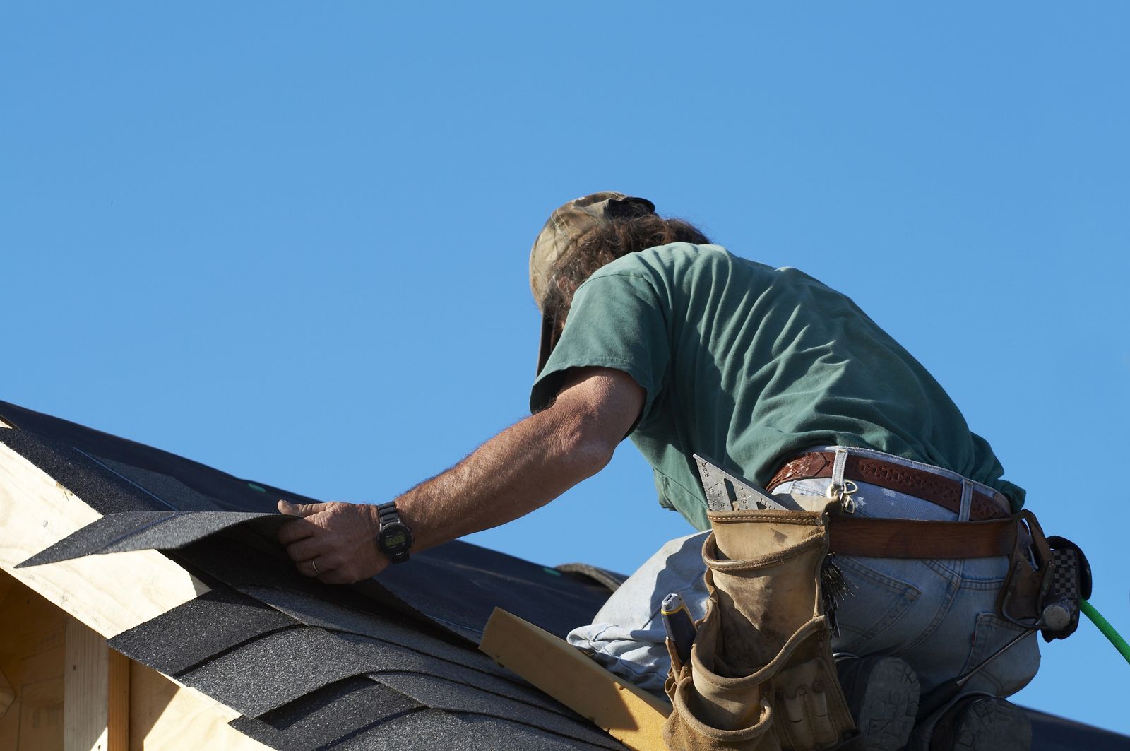 Roofer kneeling on a ridge, setting a course of architectural shingles
